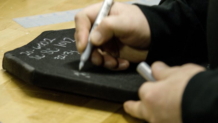 Image of HighCom employee's hands close up marking hard armor plate with numbers for a ballistics test